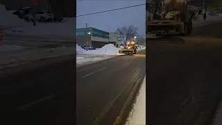 Backhoe With Plow Driving Up Boulevard