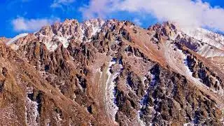 snow-covered mountain range under blue sky with clouds, ascending drone view
