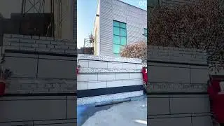 Installing speckled wall panel over brick surface using vertical measuring guide and gloved hand.