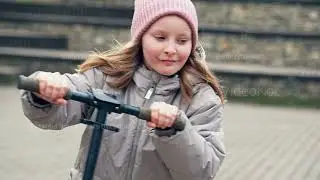 Joyful young Caucasian girl rides scooter through autumn park in slow motion