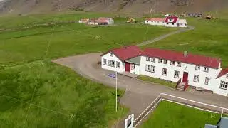 Drone view orbit around Iceland flag waving out of typical building in Iceland highland. The flag of