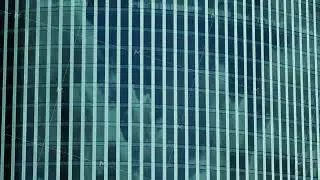Modern glass skyscraper reflecting clouds in windows forming repeating geometric pattern