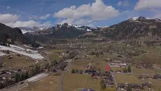 Aerial panorama capturing Gstaad Valley surrounded by towering Swiss Alpine peaks, revealing verdant