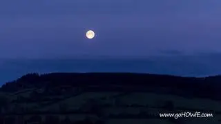 Time lapse of the full moon setting over hills at dawn