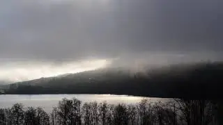 Mist is rising from wooded hills at the shore of a glittering lake in late fall - nature relaxation