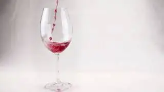Red wine is pouring into glass on white isolated background. Slow motion