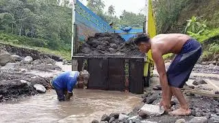 loading black sand into the truck bed by manual miners - sand mining