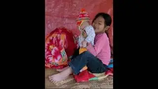 Two siblings cut small pieces of wood to build a door, lovingly caring for their little brother.