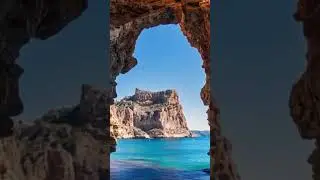 A natural rock arch frames a stunning view of a rugged cliff and turquoise sea under a clea