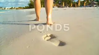 Young caucasian girl leaving footprints in the white sand of a tropical beach 2