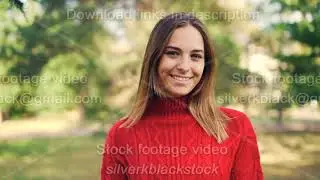 Slow motion portrait of beautiful young woman in bright red sweater standing in the park with happy