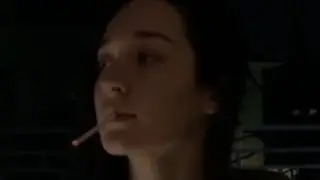 A girl smokes a cigarette on the balcony and throws the butt into the street.
