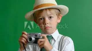 The Budding Photographer: A young, curious boy, clad in a stylish hat and tie, holds a camera,
