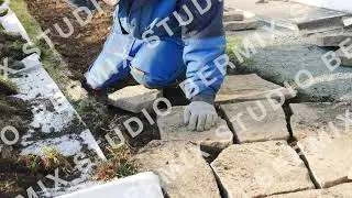 A workman's hands hits a stone with a hammer to make it fit and to place stone pavers in a row