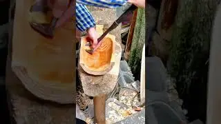 hollowing out a large piece of wood with a traditional curved tool to create a handcrafted wooden