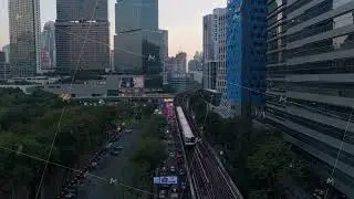 Aerial tracking view of BTS skytrain running on elevated tracks next to a busy street. Modern
