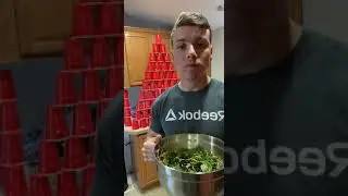 Guy shoots at cups with Nerf gun while eating a salad.