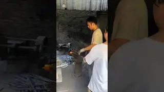 A husband-and-wife blacksmith shop, the woman watches the furnace while the man works the iron