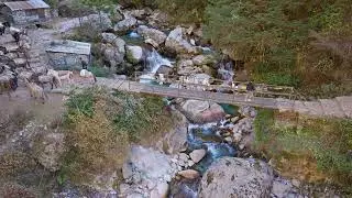 Pack animals carrying goods crossing metal bridge over mountain river, linking remote Himalayan