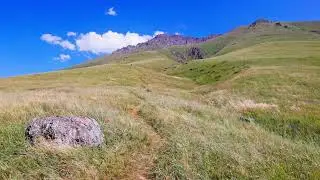 Winding pathway through grassy hill and large boulder in mountains