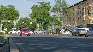 car traffic crossing city street intersection covered with green trees at sunny summer day in