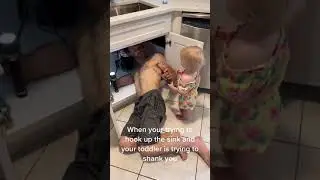 Toddler Holds Screwdriver Up At Dad While He Fixes Sink in Kitchen - 1198935