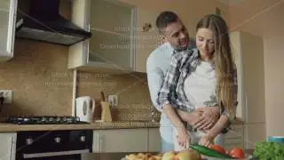 Happy young couple embracing and talking in the kitchen while cooking breakfast at home