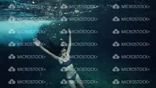 A young skinny woman in bikini floating underwater and holding her breath.