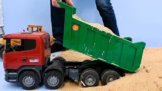 A loader carries sand in a bucket, an excavator loads a dump truck, a bulldozer is brought on a truc