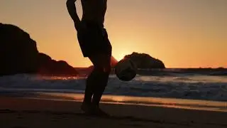 VideoVault Stock Video: Soccer player holds the ball high with his feet on the beach