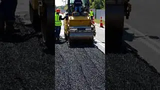 A time lapse scene of road construction, where an asphalt paving machine lays fresh black pavement.