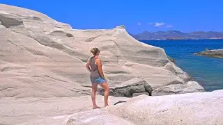 4K Woman stands on Sarakiniko cliff by turquoise blue Aegean Sea on Milos island, Greece