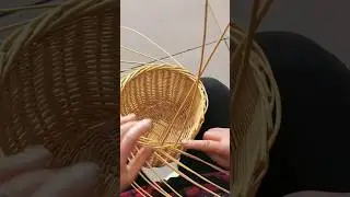 person uses their hands to weave a small, round wicker basket from light reeds