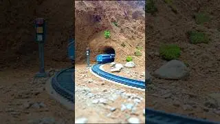 Blue Train Enters Tunnel Through Rocky Hillside with Stones on Track