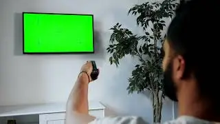 man points remote at green screen tv on wall