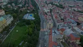 Aerial view of a street in Prague with a tram moving towards an intersection at dusk. Red tiled