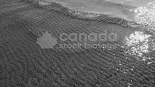 Slow motion sunlit lake water & wave with rippled sand pattern below stock video. Black & white. HD.