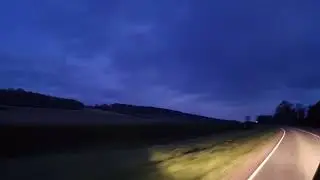 a drive in the countryside at dusk. headlights & a dark evening sky.