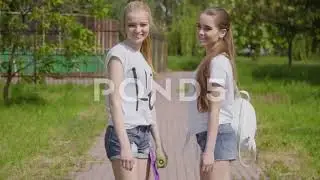 Girlfriends walking through the park and smile