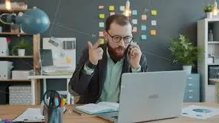 Young businessman talking on mobile phone discussing work issues and using laptop in office