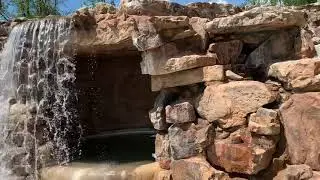 Large boulder waterfall with hidden grottoes Containing hot tubs and bar going into swimming pool .