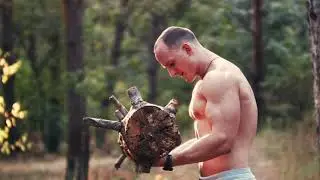 attractive shirtless muscular man lifting a heavy log in a forest upper