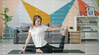Cute blonde stretching legs doing yoga at home on mat caring for body health